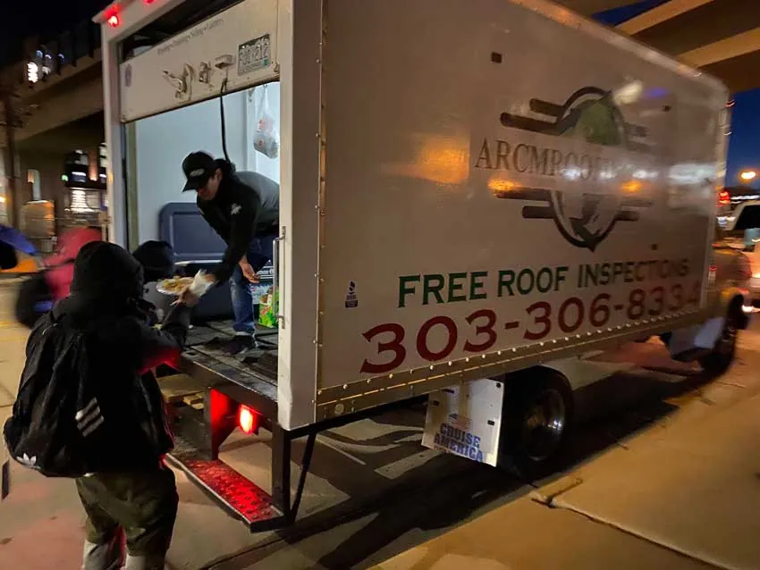 ARCM Roofing crew handing hot plates from the ARCM box truck on a Denver street at night